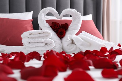 Honeymoon. Swans made with towels and beautiful rose petals on bed in room