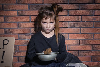 Photo of Poor little girl with bread against brick wall