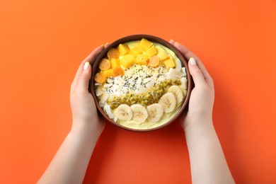 Woman holding tasty smoothie bowl with fresh fruits at orange table, top view