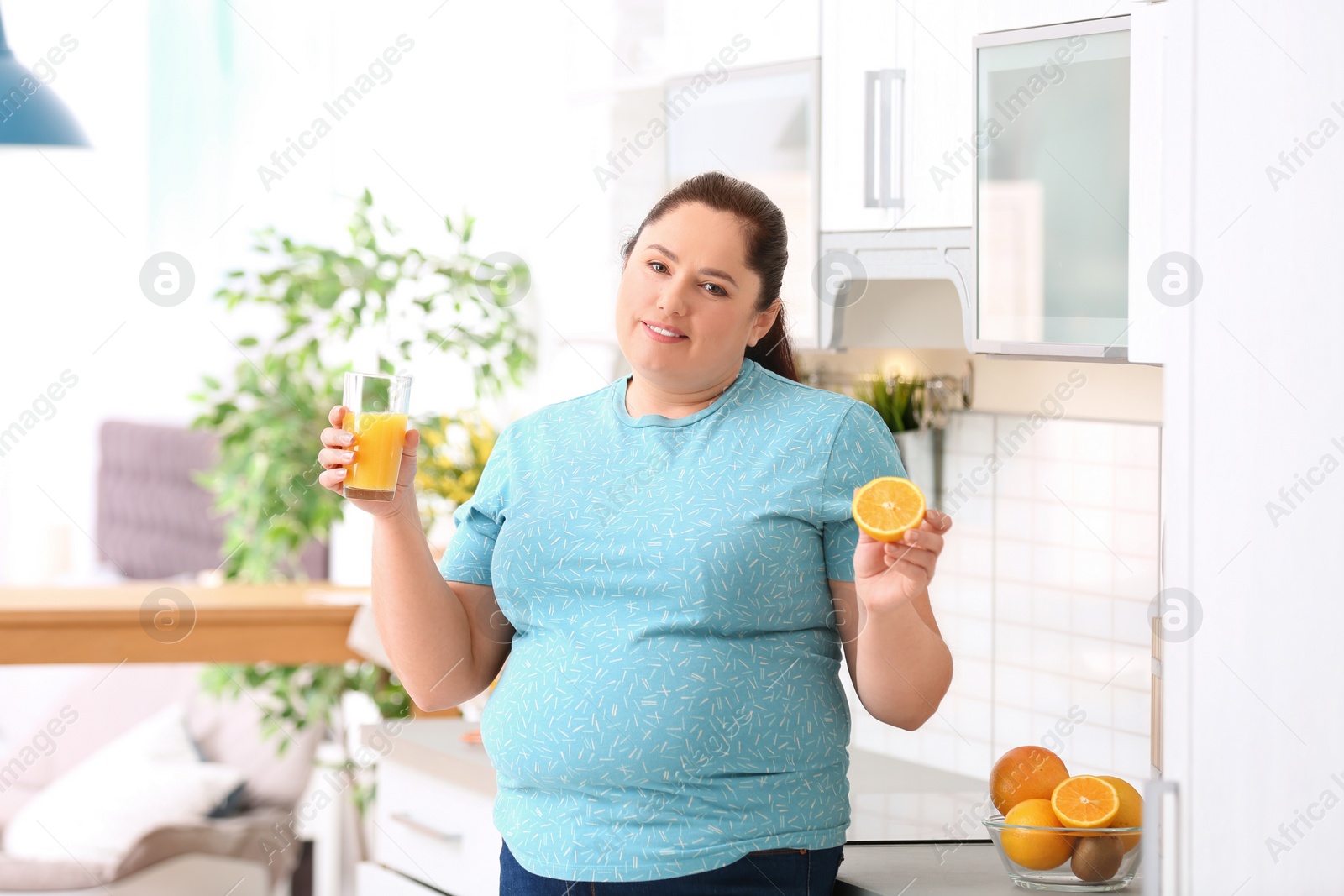 Photo of Overweight woman with glass of fresh juice and orange in kitchen. Healthy diet