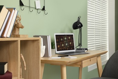 Photo of Workplace with modern laptop on wooden desk and bookcase at home