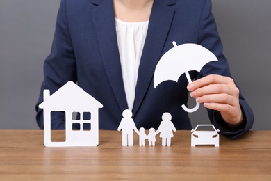 Photo of Woman with cutout paper family, house, car and umbrella at table, closeup. Life insurance concept