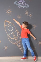 Photo of Cute little child playing with chalk rocket drawing on grey wall