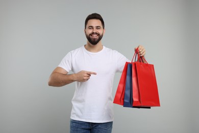 Photo of Happy man pointing at many paper shopping bags on grey background