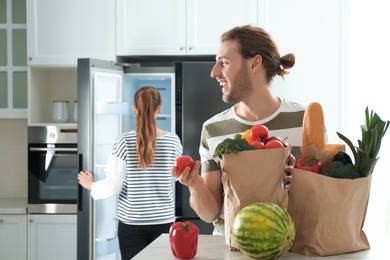 Man with fresh products at table and woman near refrigerator in kitchen