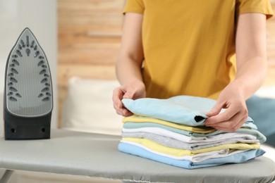 Photo of Woman with folded clothes after ironing near board at home, closeup