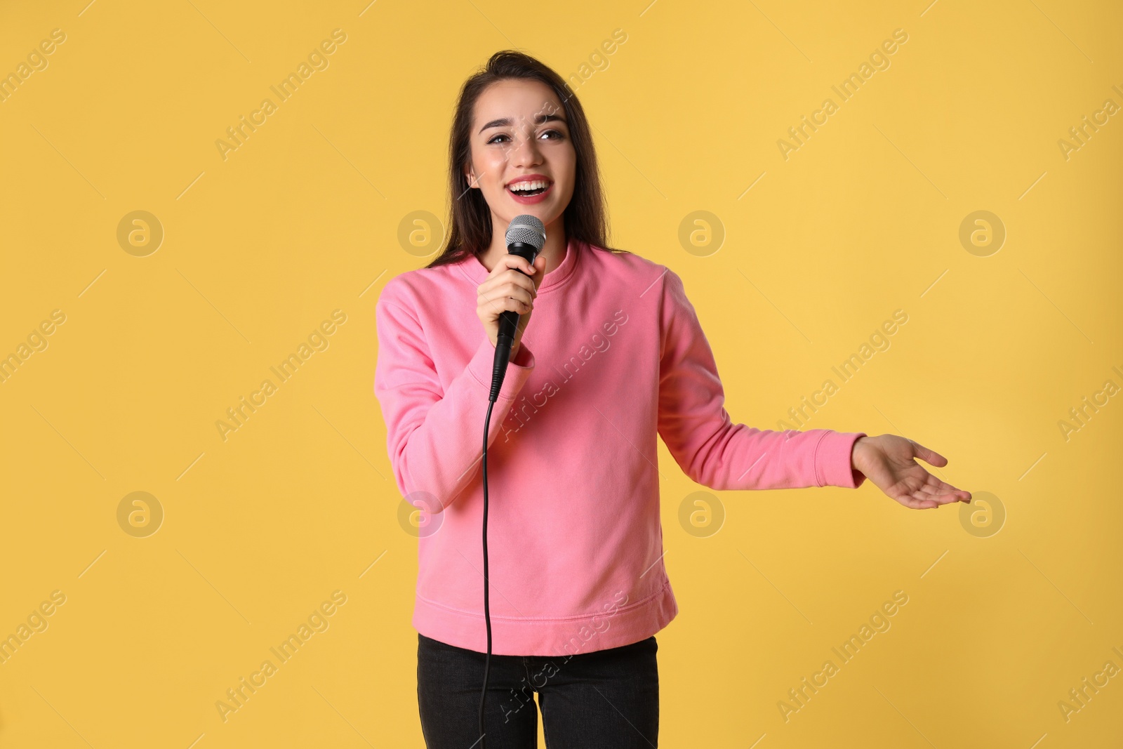 Photo of Young woman in casual clothes posing with microphone on color background