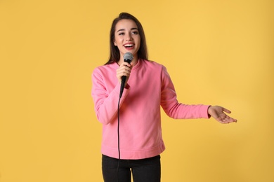 Young woman in casual clothes posing with microphone on color background