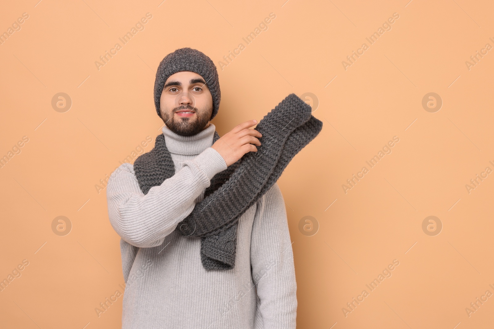 Photo of Smiling man in knitted scarf and hat on beige background. Space for text