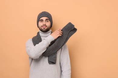 Smiling man in knitted scarf and hat on beige background. Space for text