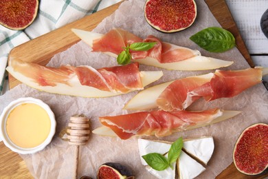 Photo of Tasty melon, jamon and figs served on wooden board, flat lay