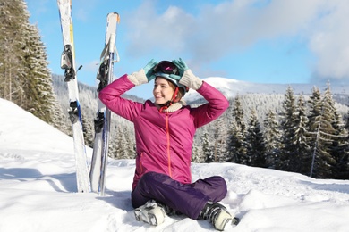 Photo of Happy young woman with ski equipment sitting on snow in mountains. Winter vacation