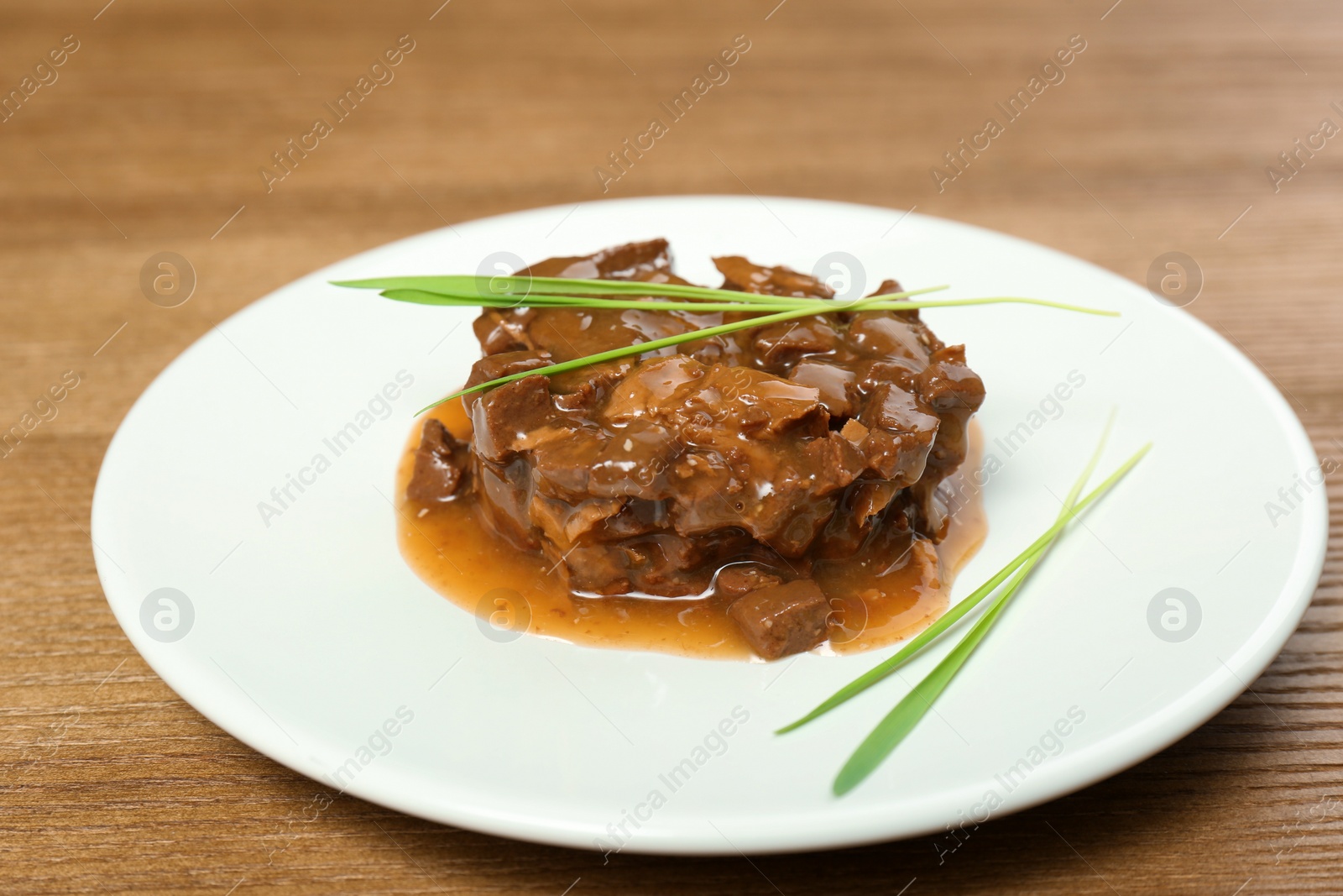 Photo of Plate with wet pet food and grass on wooden table