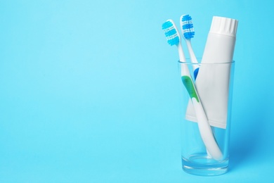 Photo of Glass with brushes and toothpaste on color background. Space for text