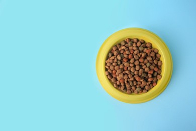 Dry pet food in feeding bowl on light blue background, top view. Space for text