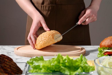 Photo of Woman making delicious vegetarian burger at white marble table, closeup