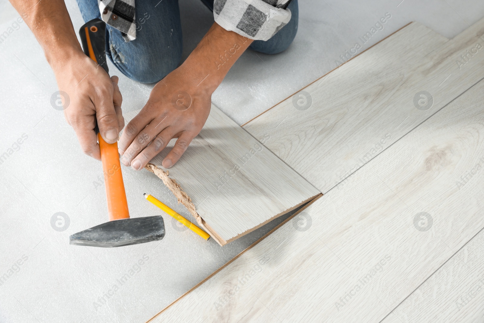 Photo of Professional worker using hammer during installation of new laminate flooring, closeup