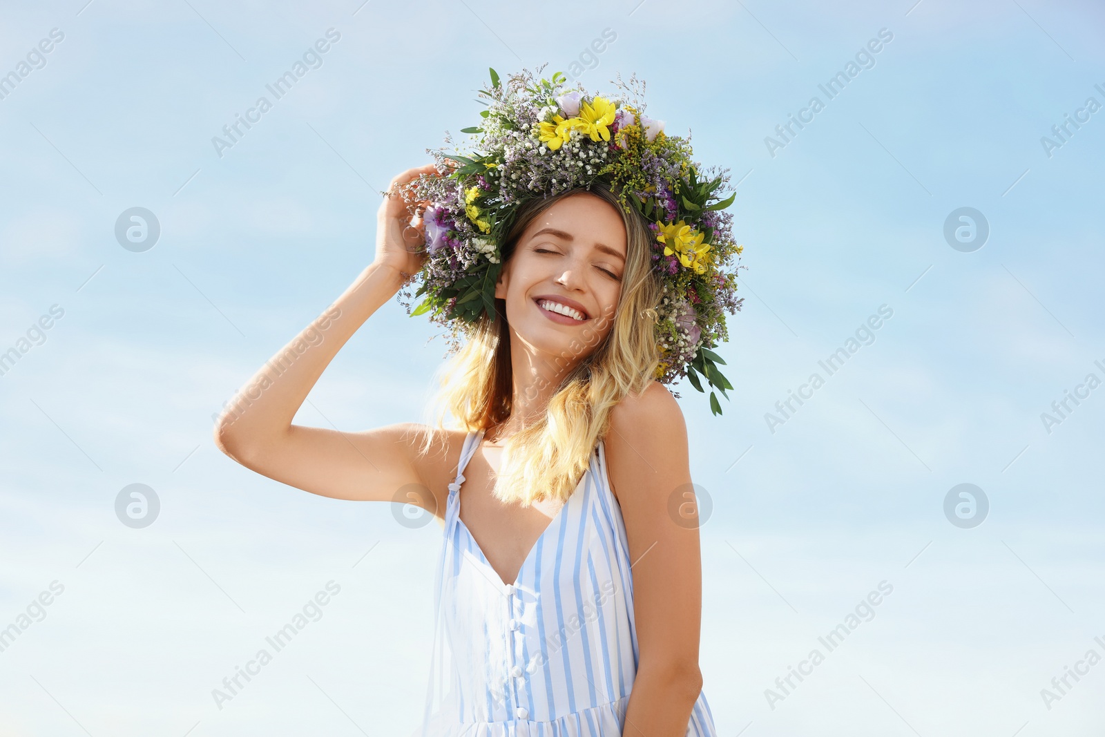 Photo of Young woman wearing wreath made of beautiful flowers outdoors on sunny day