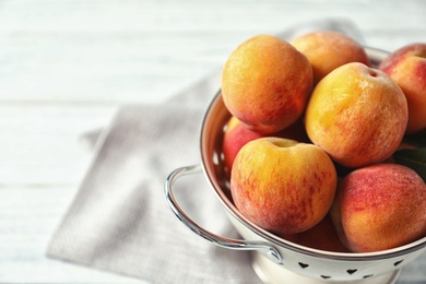 Colander with delicious ripe peaches on table