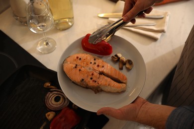 Man holding plate with tasty salmon steak and vegetables cooked on frying pan, above view