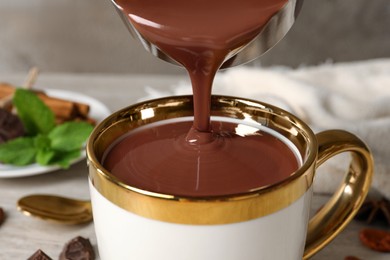 Pouring yummy hot chocolate into cup on table, closeup