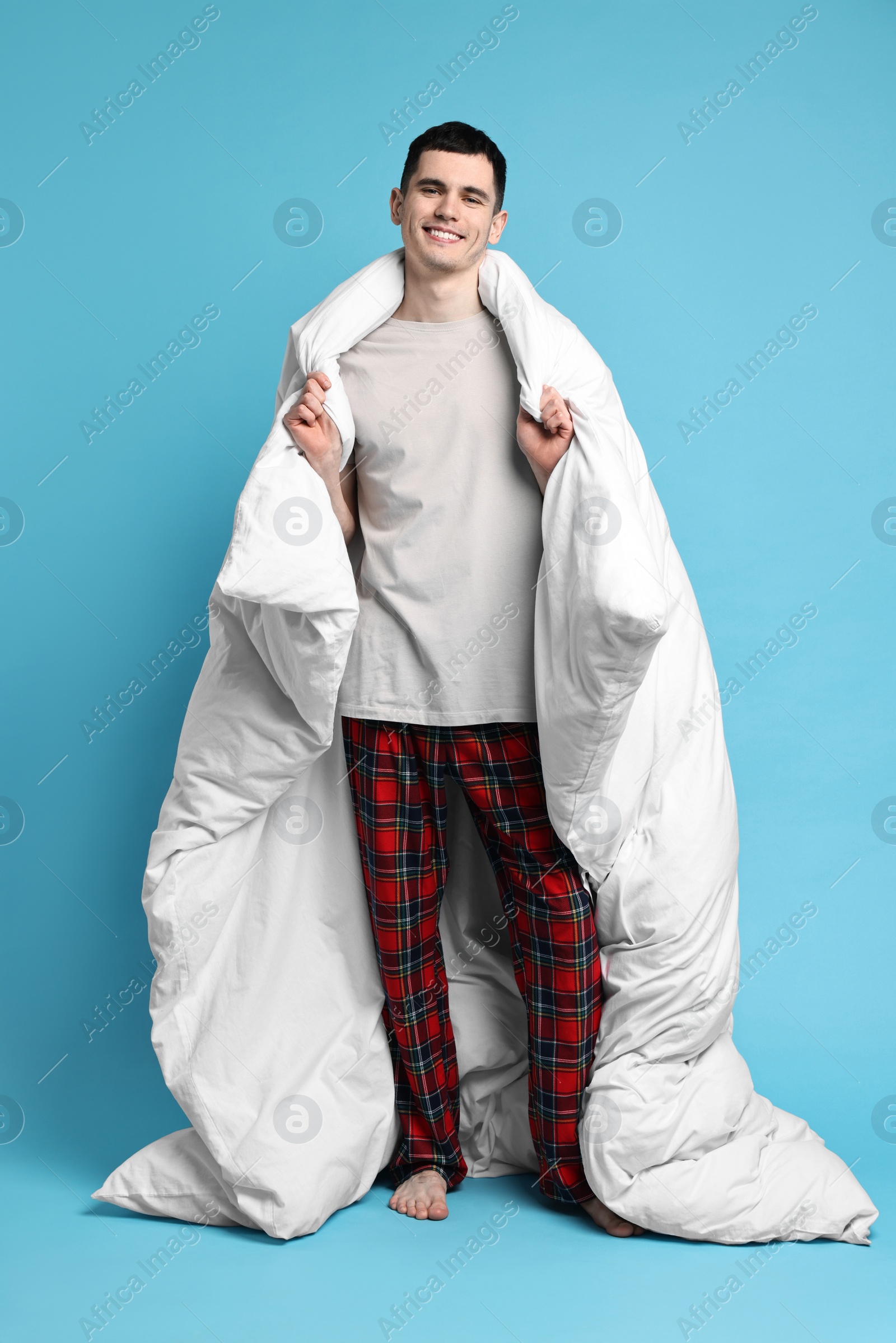 Photo of Happy man in pyjama wrapped in blanket on light blue background