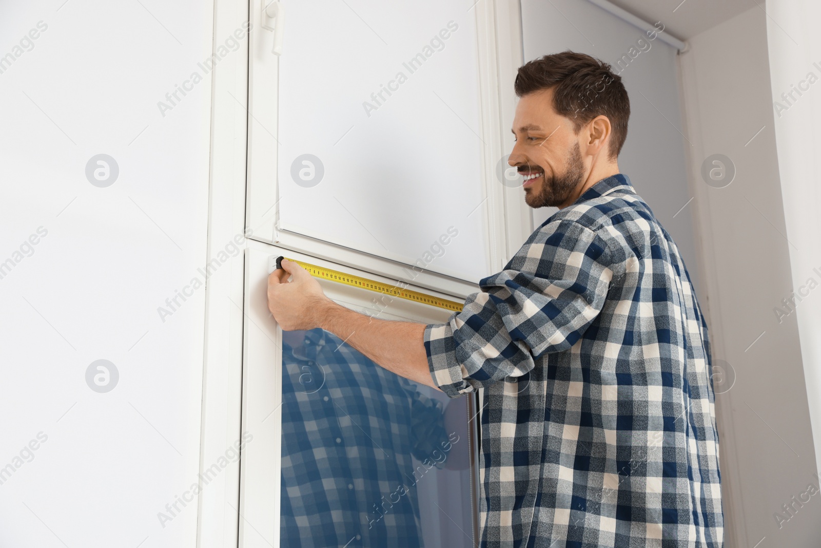 Photo of Man measuring window with tape indoors. Roller blinds installation