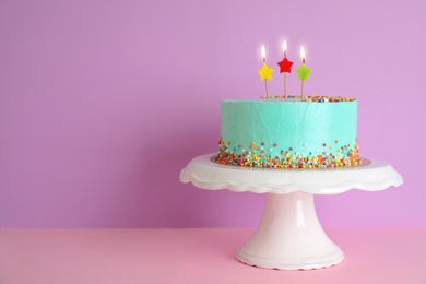 Fresh delicious birthday cake with candles on stand against color background. Space for text