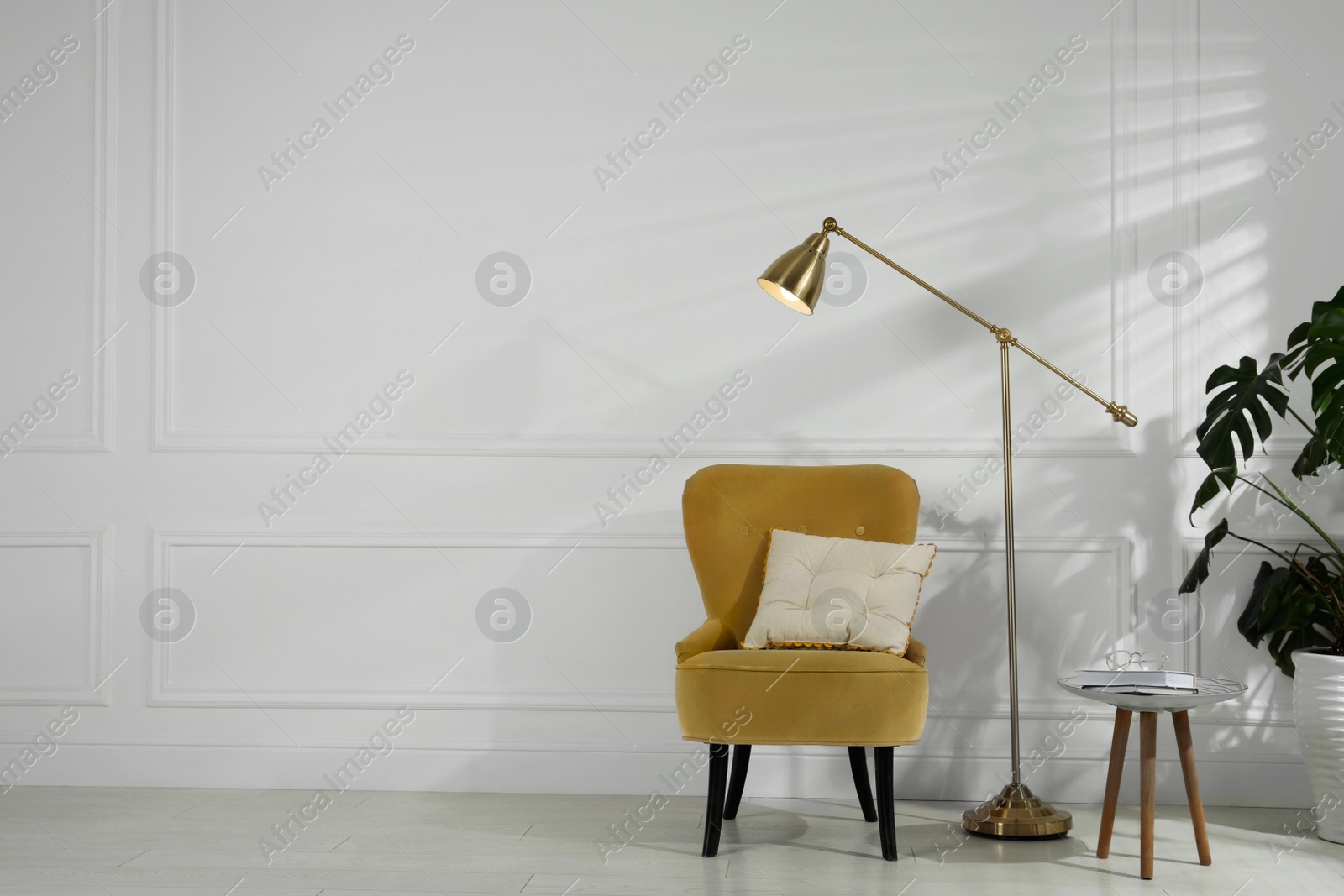 Photo of Comfortable armchair, table, floor lamp and houseplant near white wall in room, space for text. Interior design