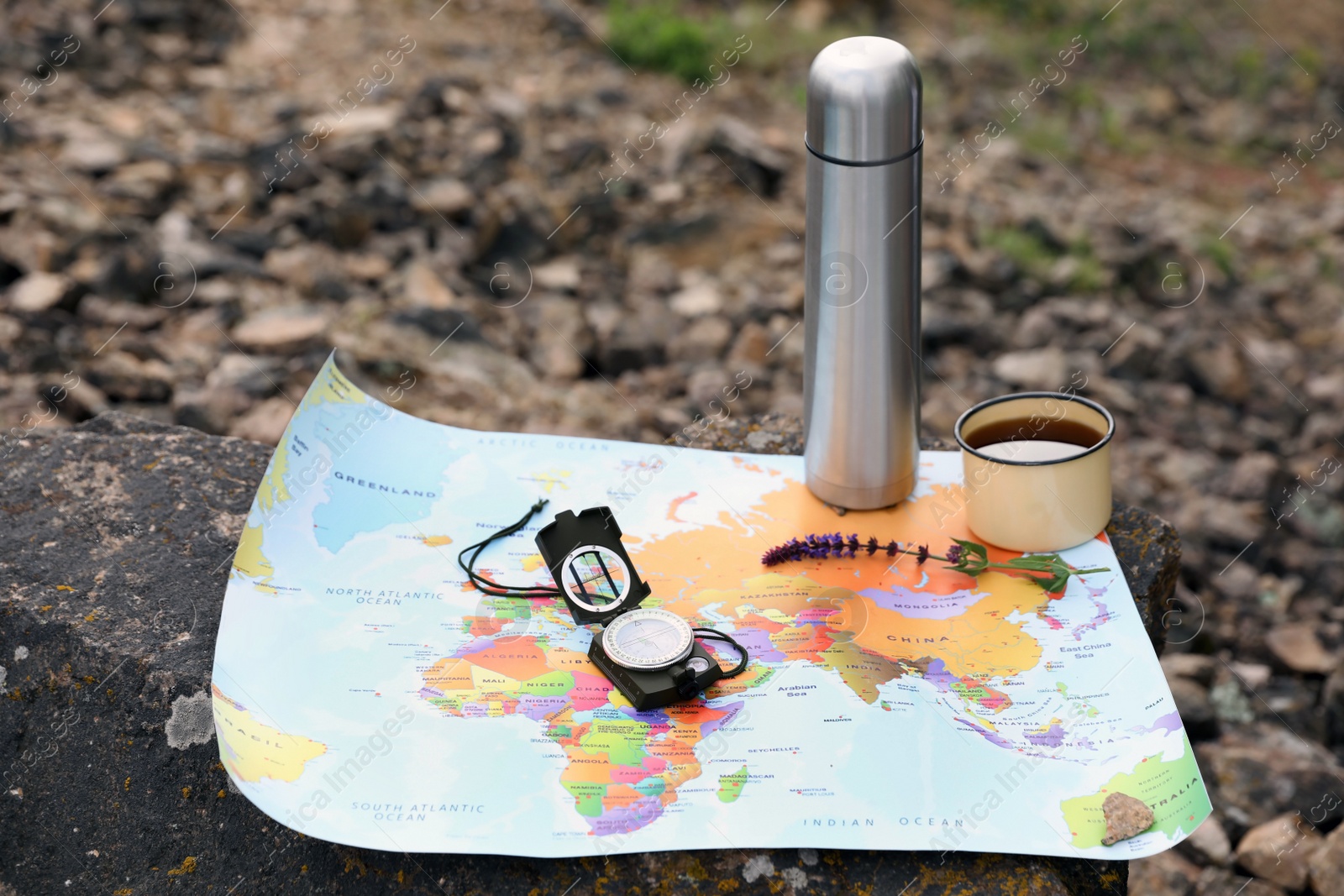 Photo of Compass, mug, thermos and map on rock outdoors. Camping season