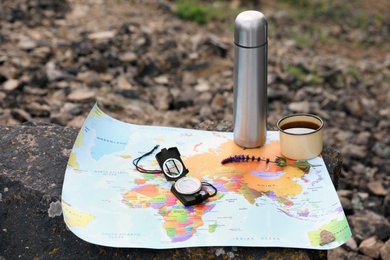 Compass, mug, thermos and map on rock outdoors. Camping season