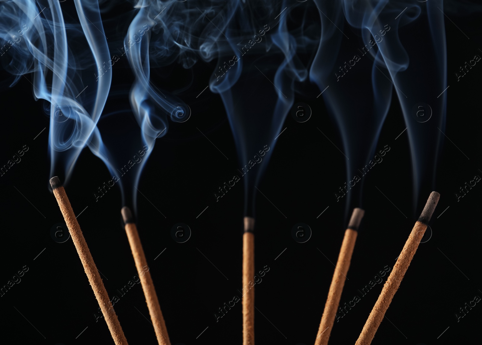 Photo of Incense sticks smoldering on black background, closeup