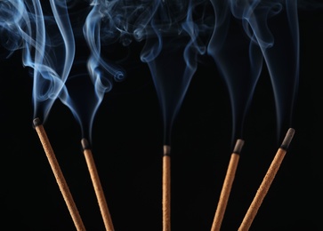 Incense sticks smoldering on black background, closeup