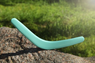 Sunlit turquoise wooden boomerang on stone outdoors