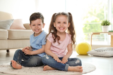 Photo of Cute children sitting on carpet in living room