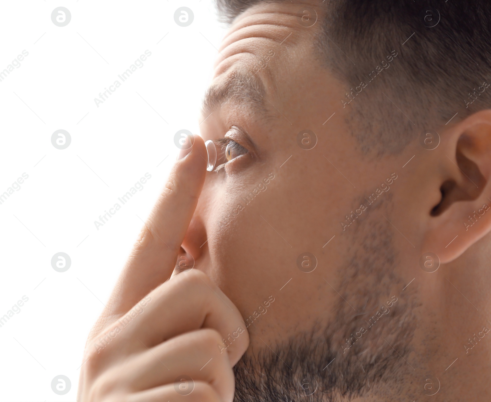 Photo of Young putting contact lens in his eye on white background, closeup