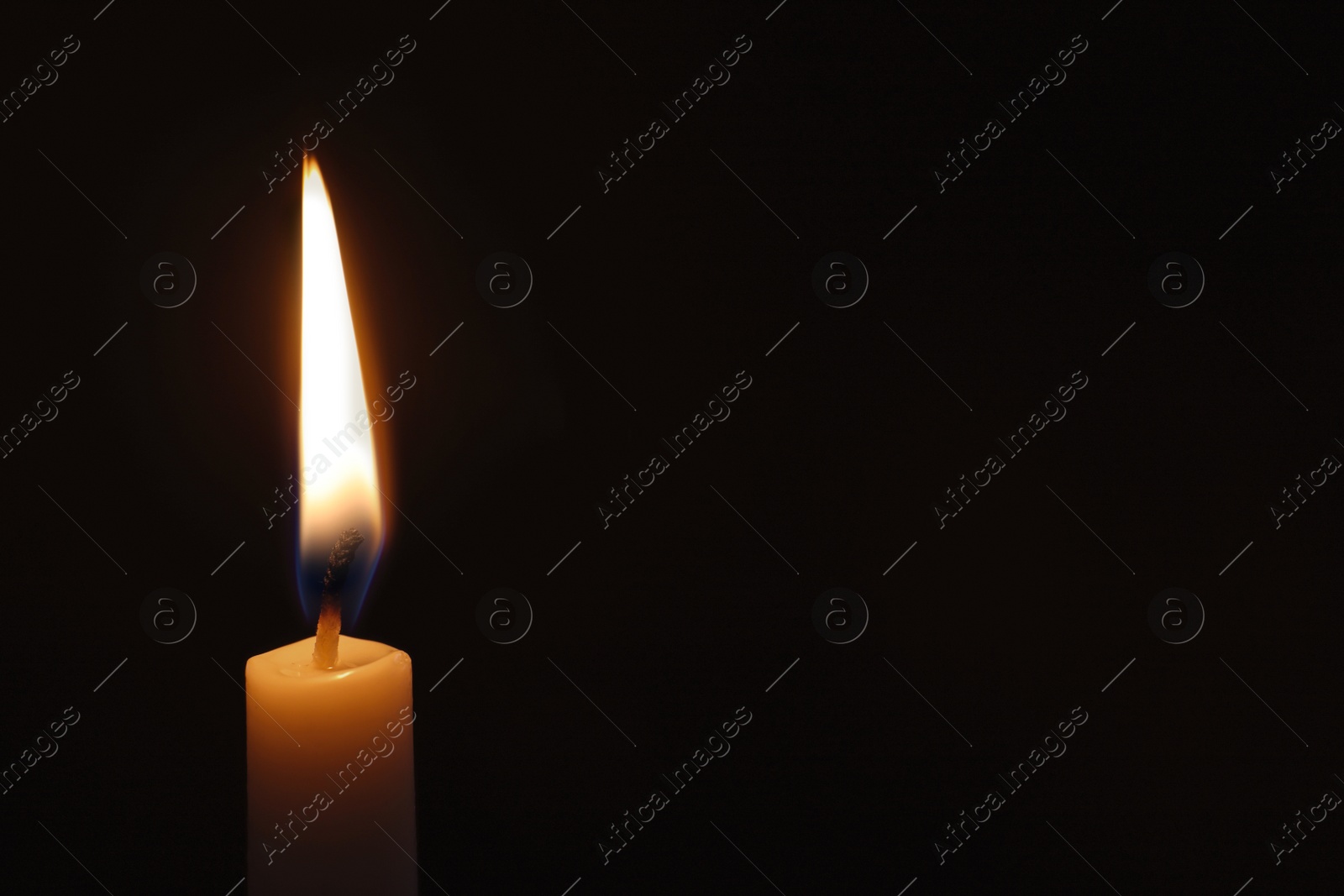 Photo of Wax candle burning on black background, closeup