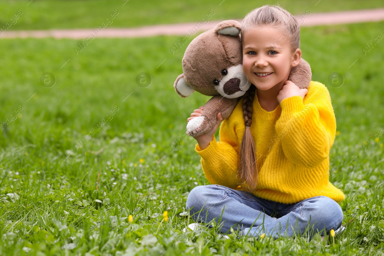 Photo of Little girl with teddy bear on green grass outdoors. Space for text