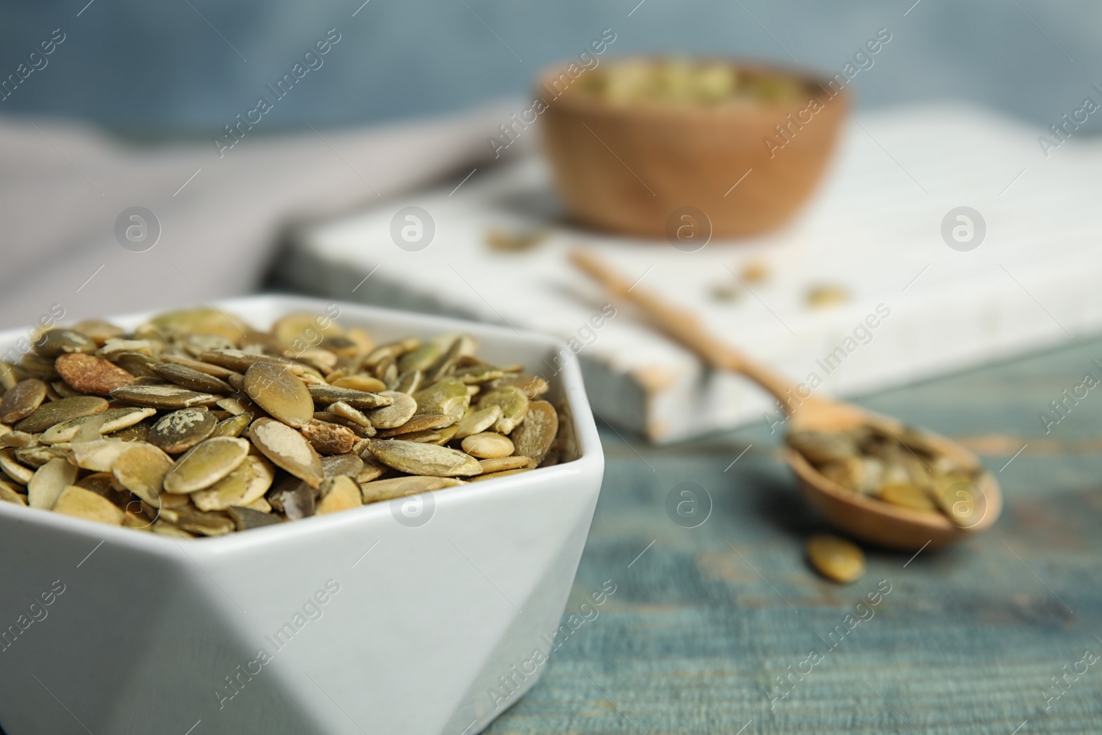 Photo of Bowl of raw pumpkin seeds on blue wooden table, closeup. Space for text