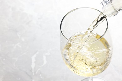 Pouring tasty aromatic wine in glass at gray marble table, closeup. Space for text