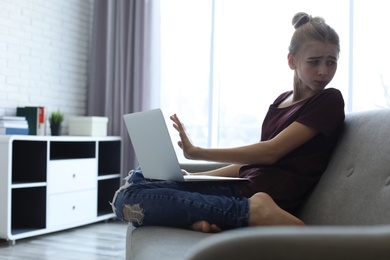 Photo of Terrified teenage girl with laptop in room. Danger of internet