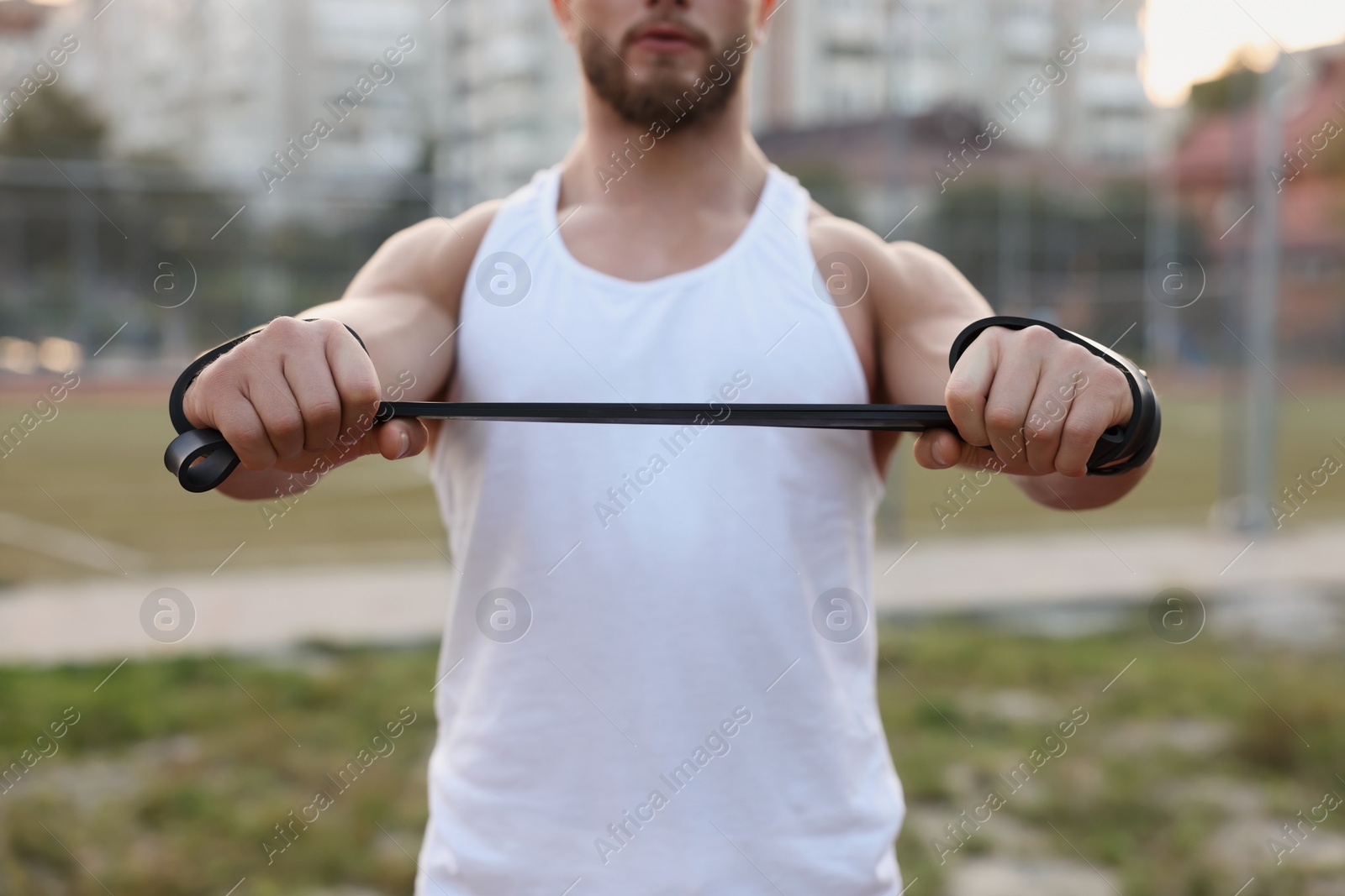 Photo of Muscular man doing exercise with elastic resistance band outdoors, closeup