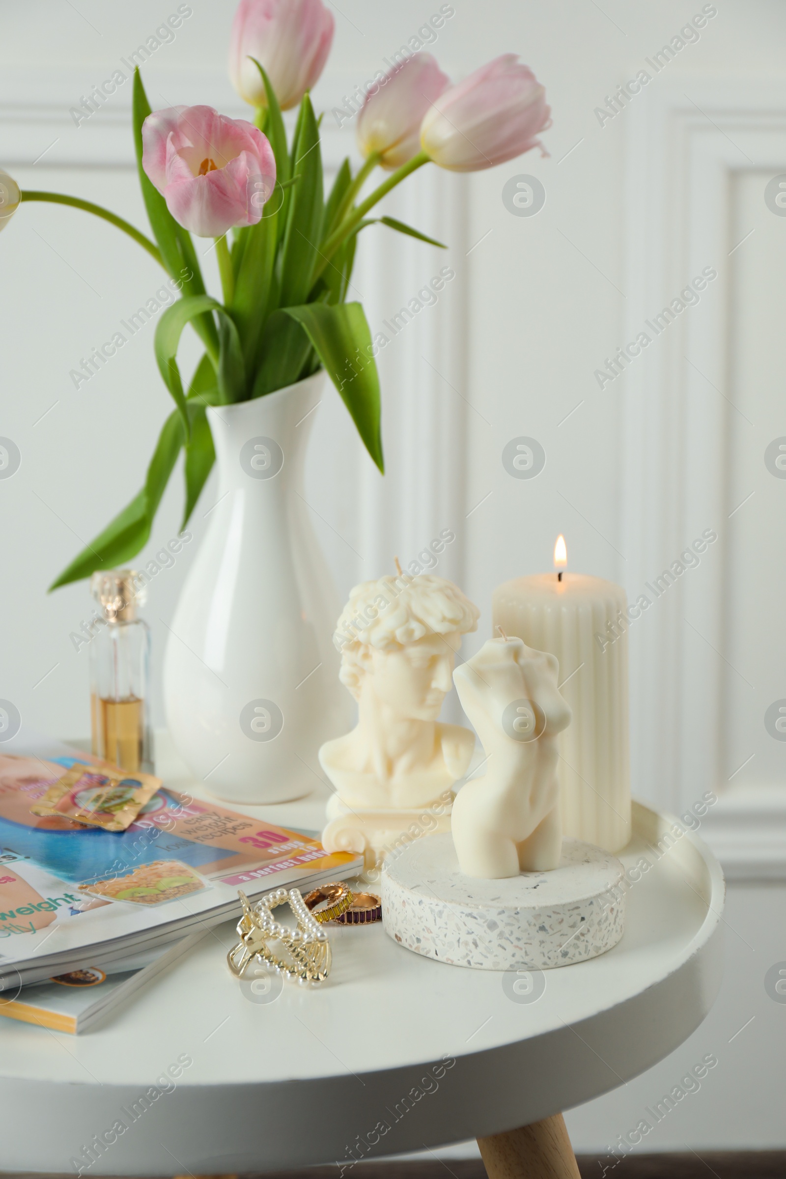 Photo of Different beautiful candles and tulips on white table. Stylish decor