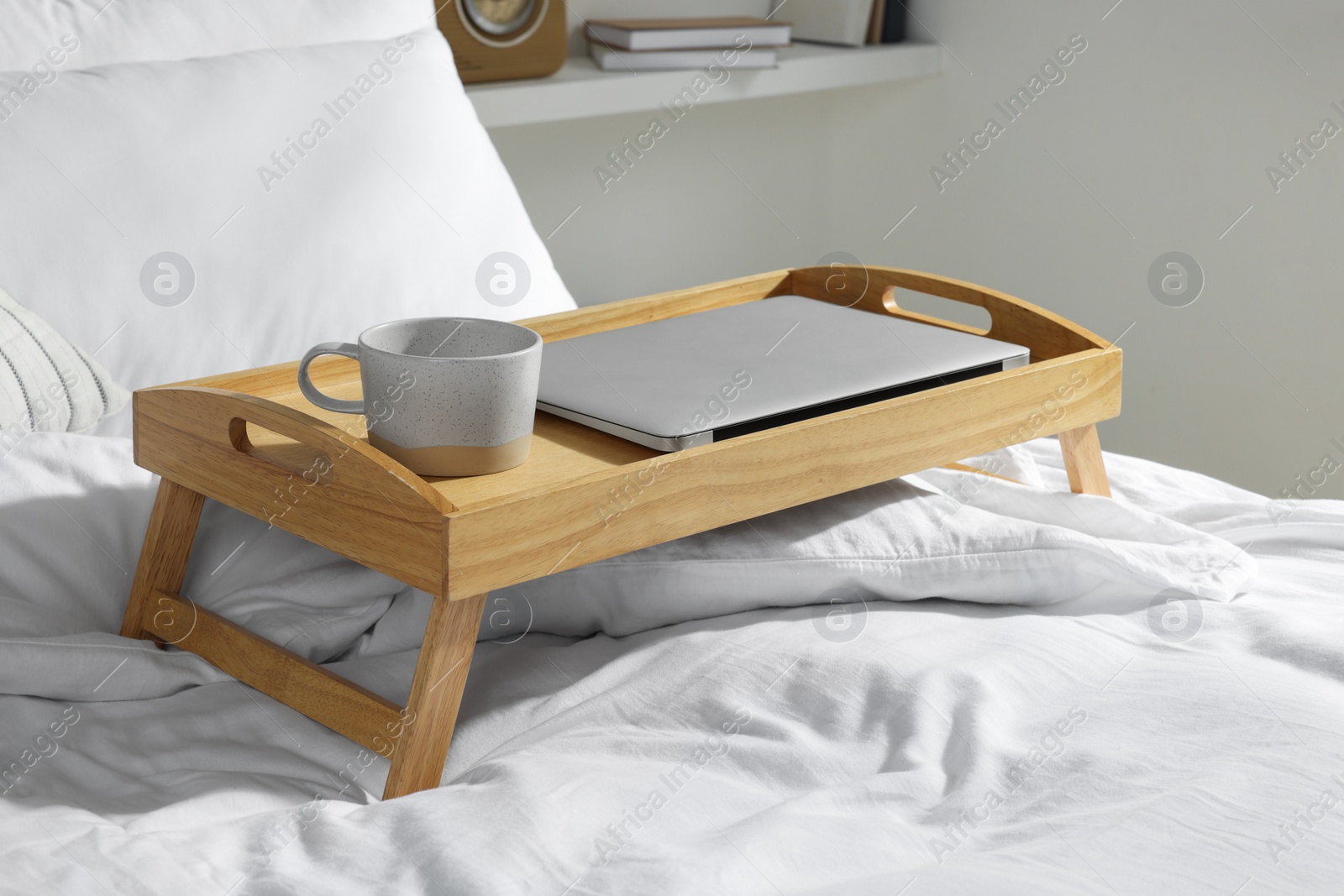 Photo of Wooden tray with modern laptop and cup of aromatic drink on bed indoors