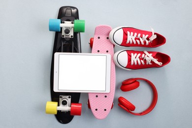 Modern tablet, headphones, skateboards and shoes on light grey background, flat lay. Space for text