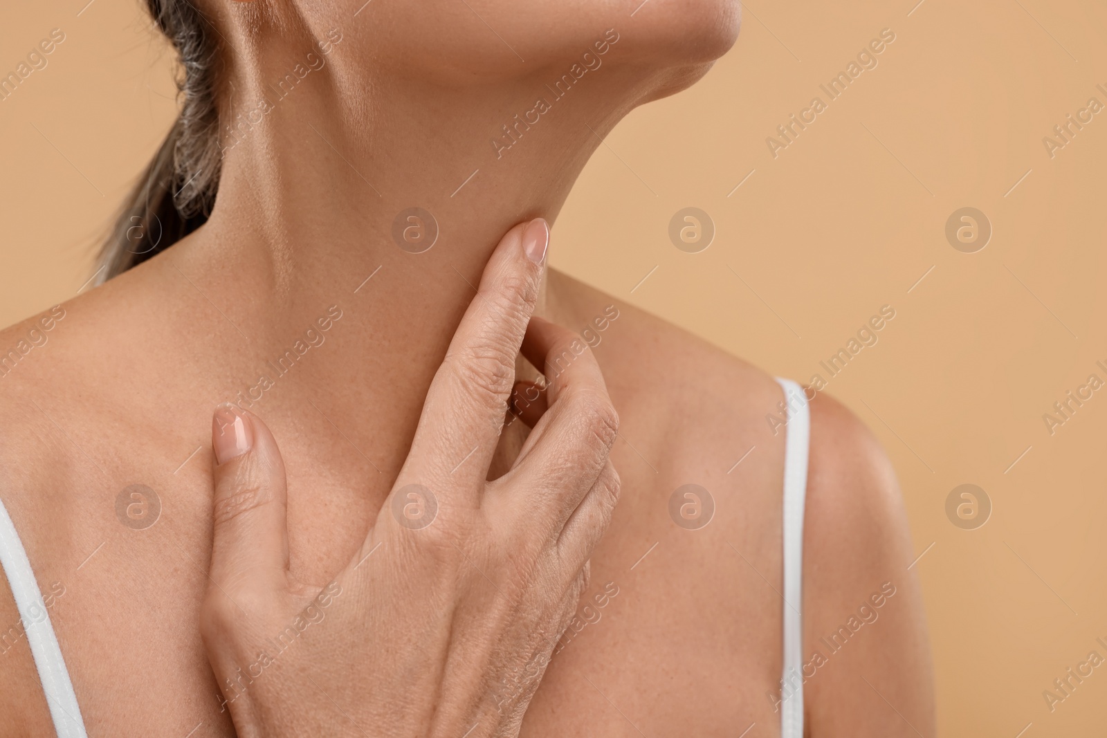 Photo of Mature woman touching her neck on beige background, closeup