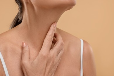 Photo of Mature woman touching her neck on beige background, closeup