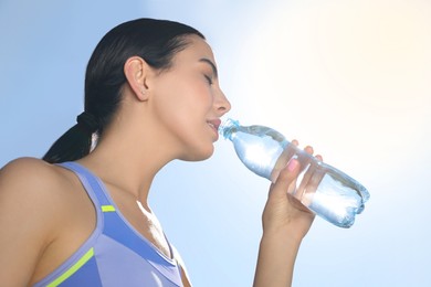 Photo of Beautiful young sportswoman drinking water outdoors, closeup. Refreshing drink