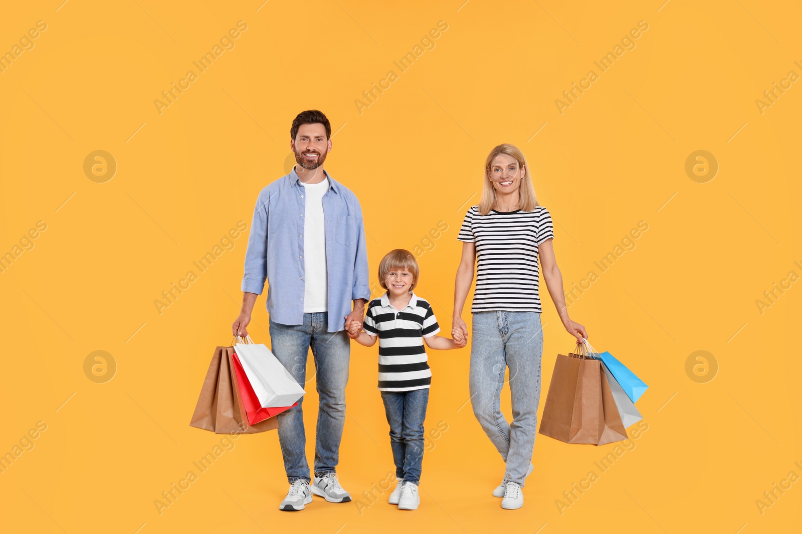 Photo of Family shopping. Happy parents and son with paper bags on orange background
