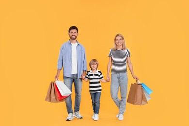 Family shopping. Happy parents and son with paper bags on orange background